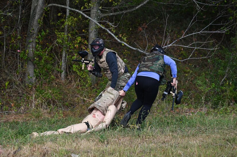 Airmen dragging a medical mannequin while shooting paintball guns.