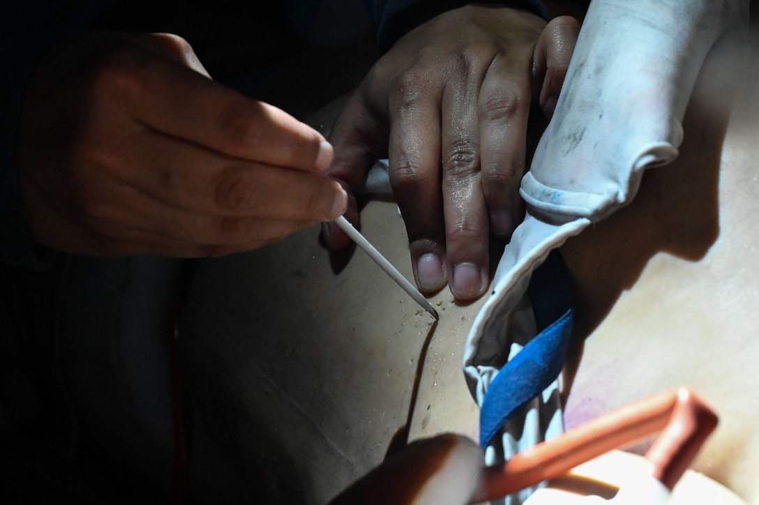 Airman puncturing a medical mannequin with a needle.