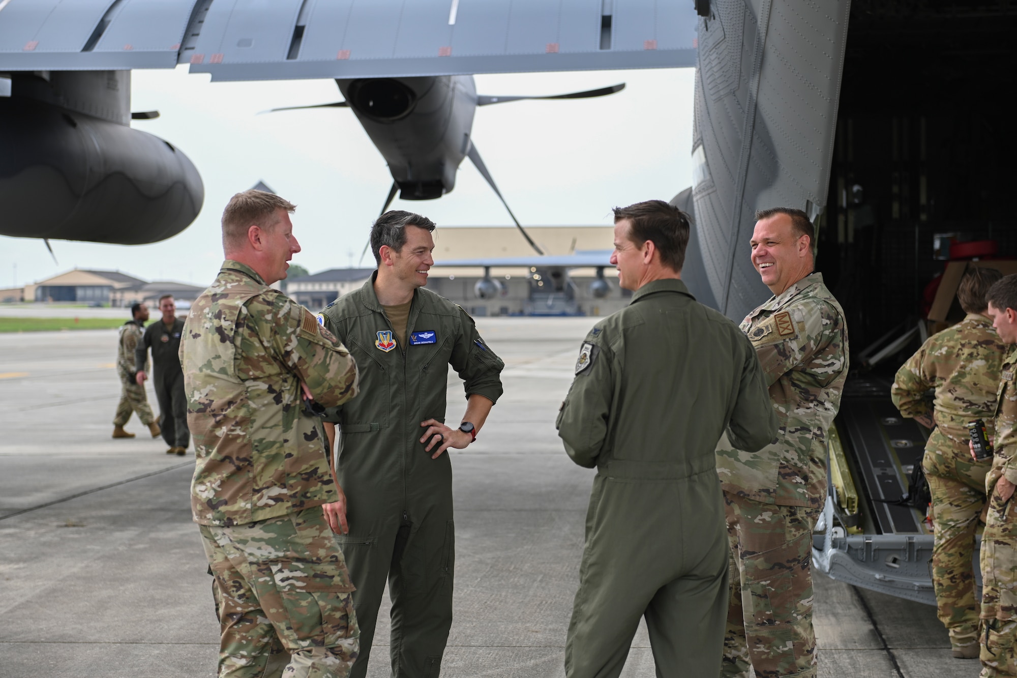 A photo of four people standing in a circle laughing, standing behind an HC-130J Combat King II.