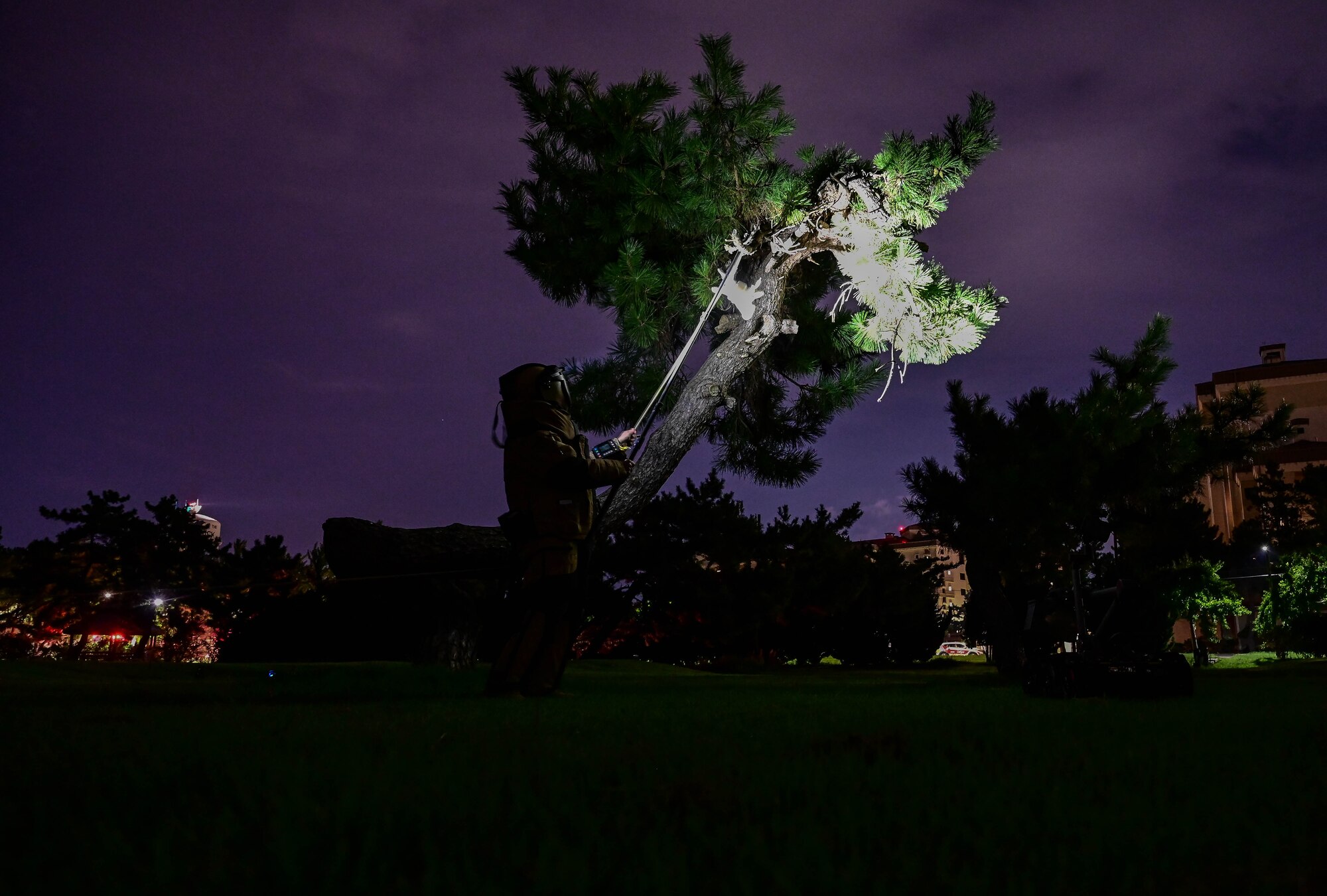 Man in bomb suit at night stands under tree.