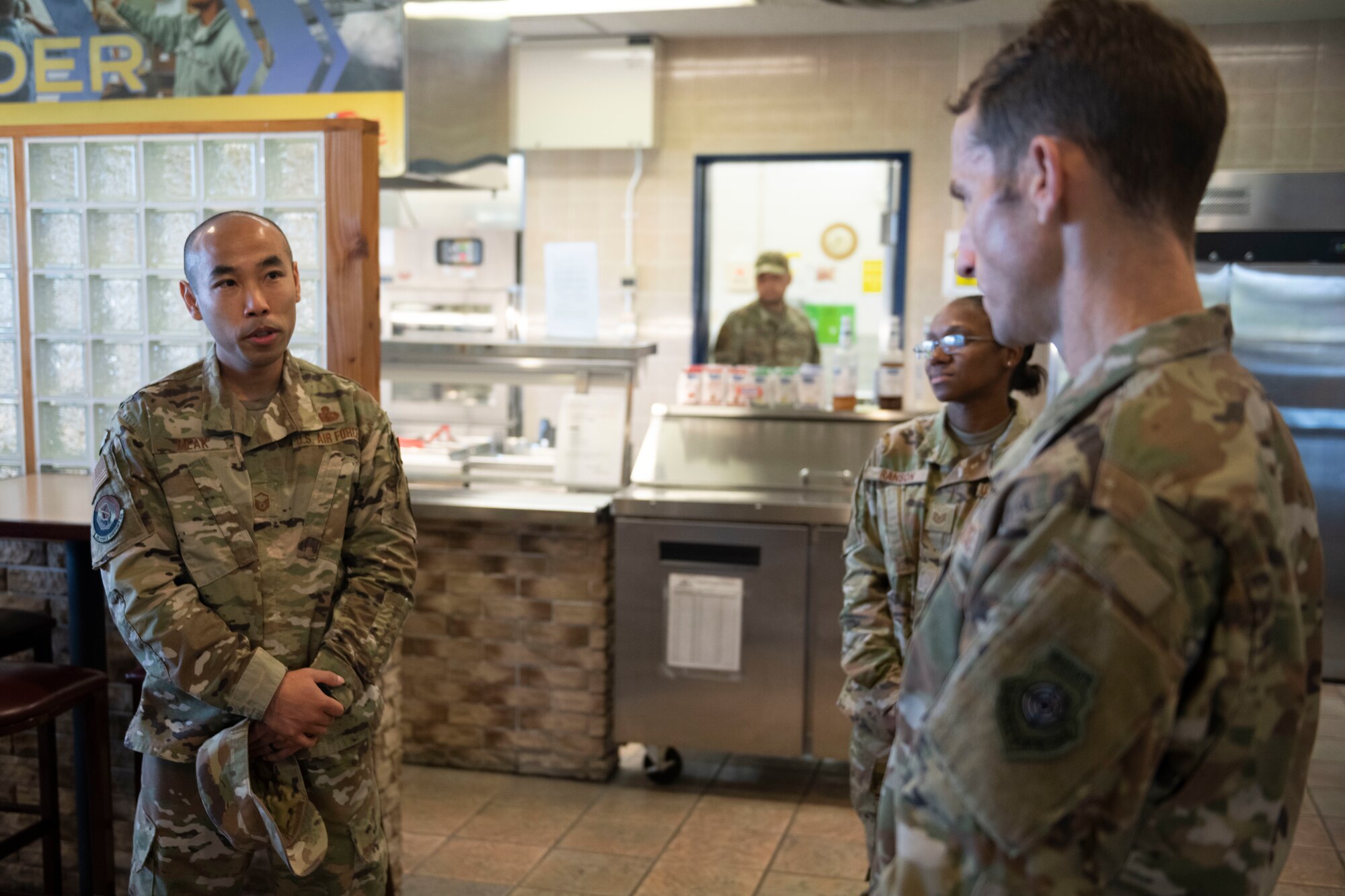 Military members in uniform stand in a dining facility talking
