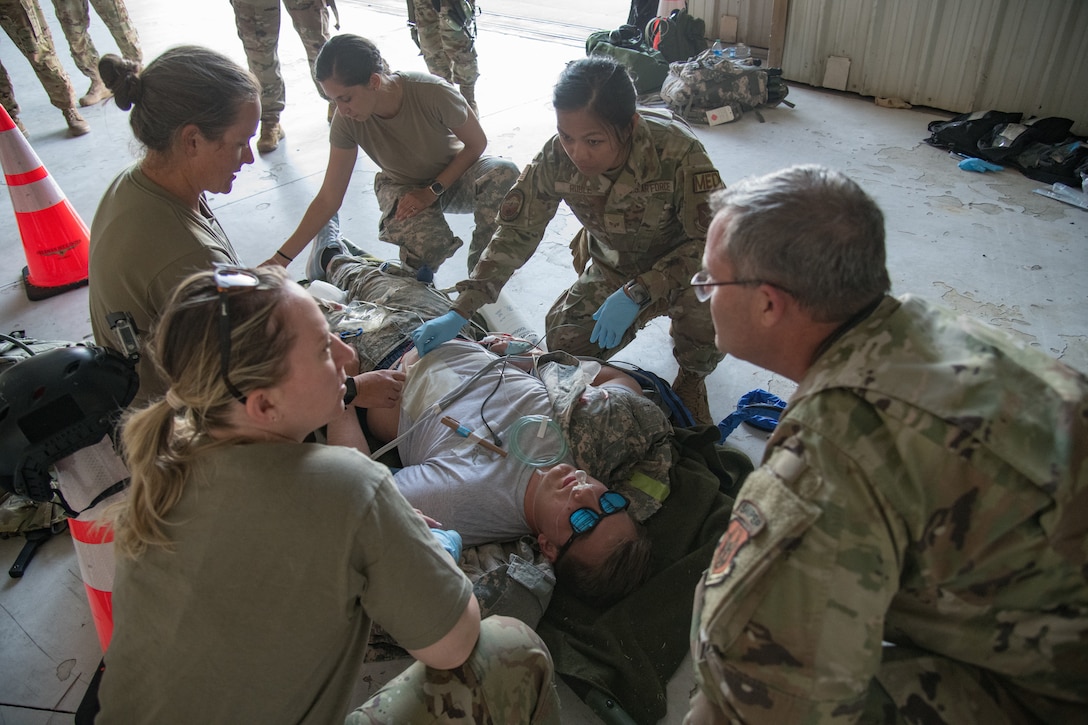 Five uniformed Airmen gathered around a person with fake injuries laying on a litter.