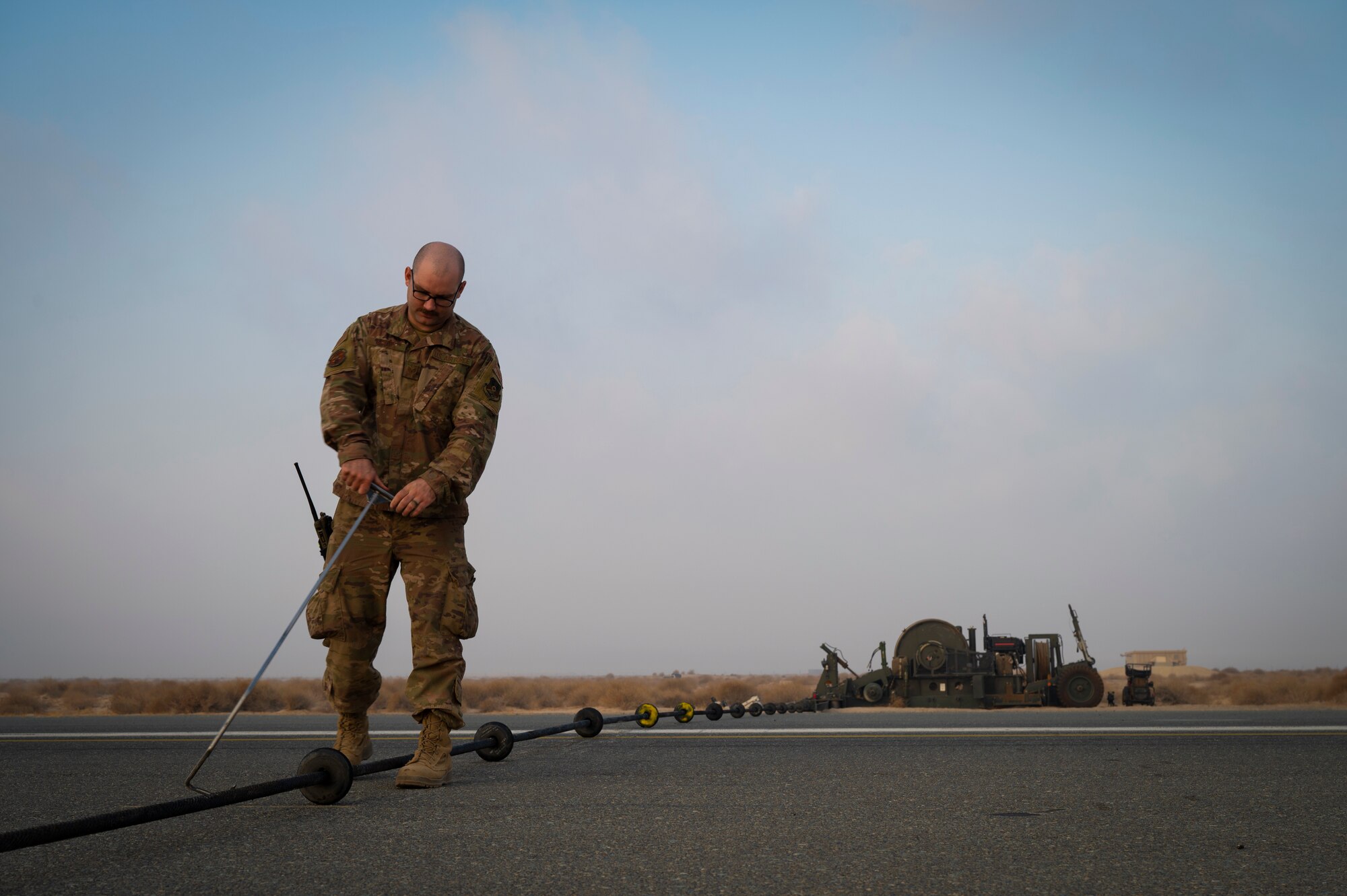 U.S. Air Force Staff Sgt. Ryan Moore, 386th Expeditionary Civil Engineer Squadron electrical power production craftsman, spaces out rubber donuts across the pendant cable for the Mobile Aircraft Arresting System during a routine check in the midst of Operation Agile Spartan III at an undisclosed location, September 8, 2022. OAS III tested Ninth Air Force (Air Forces Central)’s ability to execute rapid troop and equipment movement to and from dispersed locations around the U.S. Central Command area of responsibility. (U.S. Air Force photo by Staff Sgt. Dalton Williams)