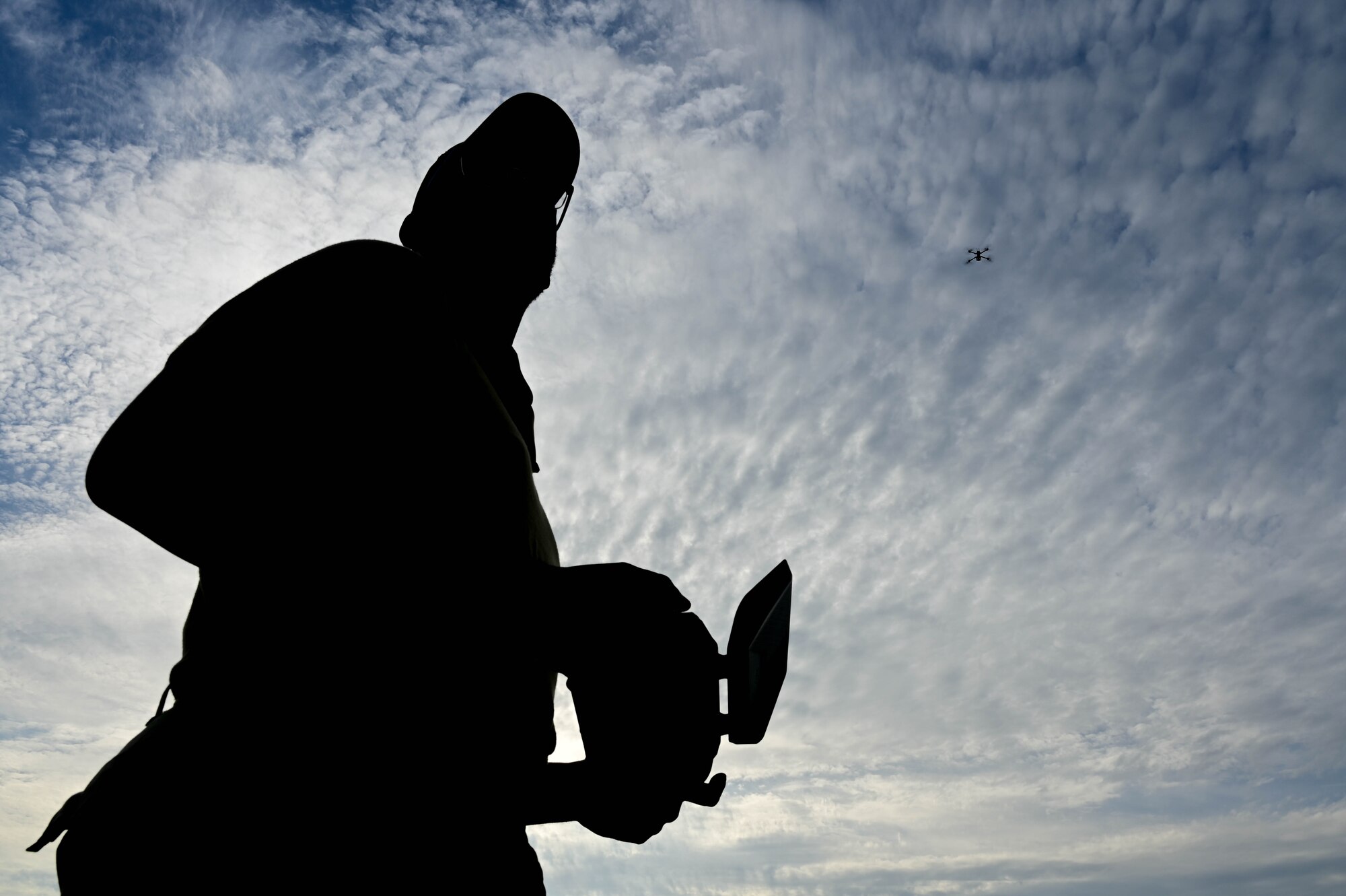 Silhouette of man holding controller with drone flying behind him.