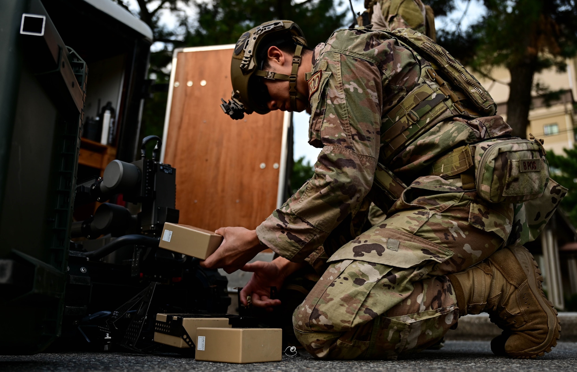 Kneeling military member places battery pack into robot.