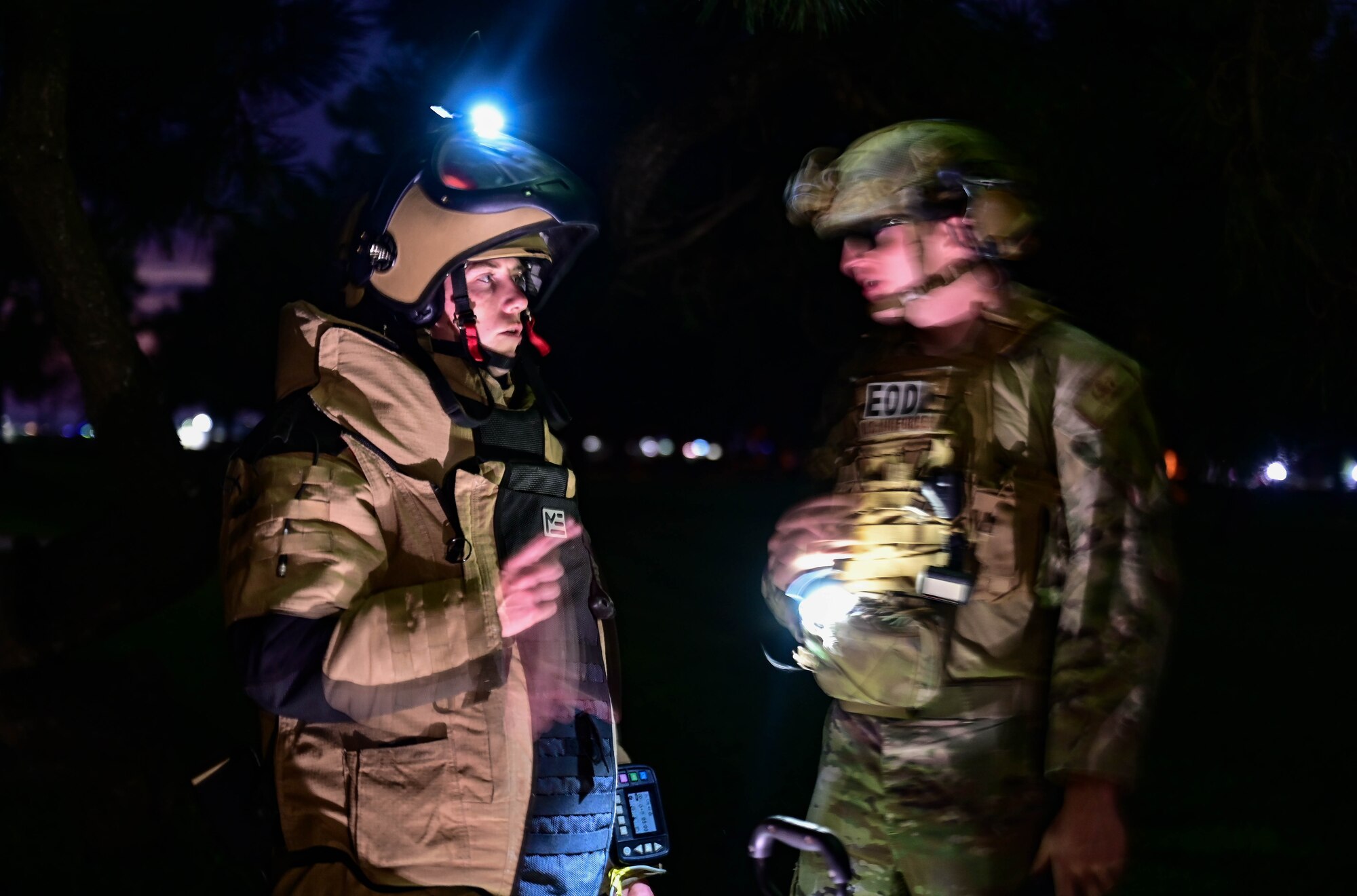 Two men in military clothing speak at night.