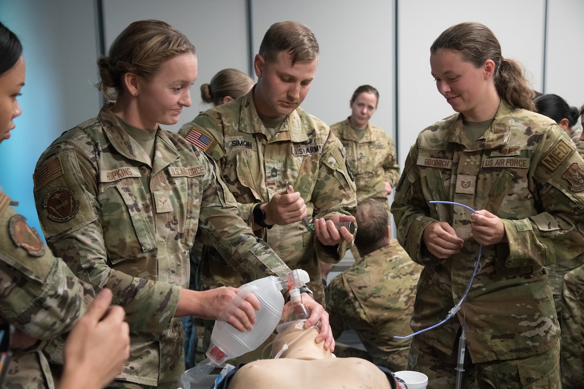 Three uniformed servicemembers surround a medical training mannequin and practice using a ventilator.