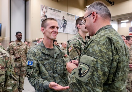 Pvt. Sead Berisha, a psychological operations soldier with the Kosovo Security Force, smiles as he receives his Air Assault badge from Lt. Col. Berat Shala, executive officer to the KSF commander, at Camp Dodge in Johnston, Iowa, Sept. 9, 2022. Over 200 students participated in the 12-day course, which trains service members in sling load operations and rappelling.