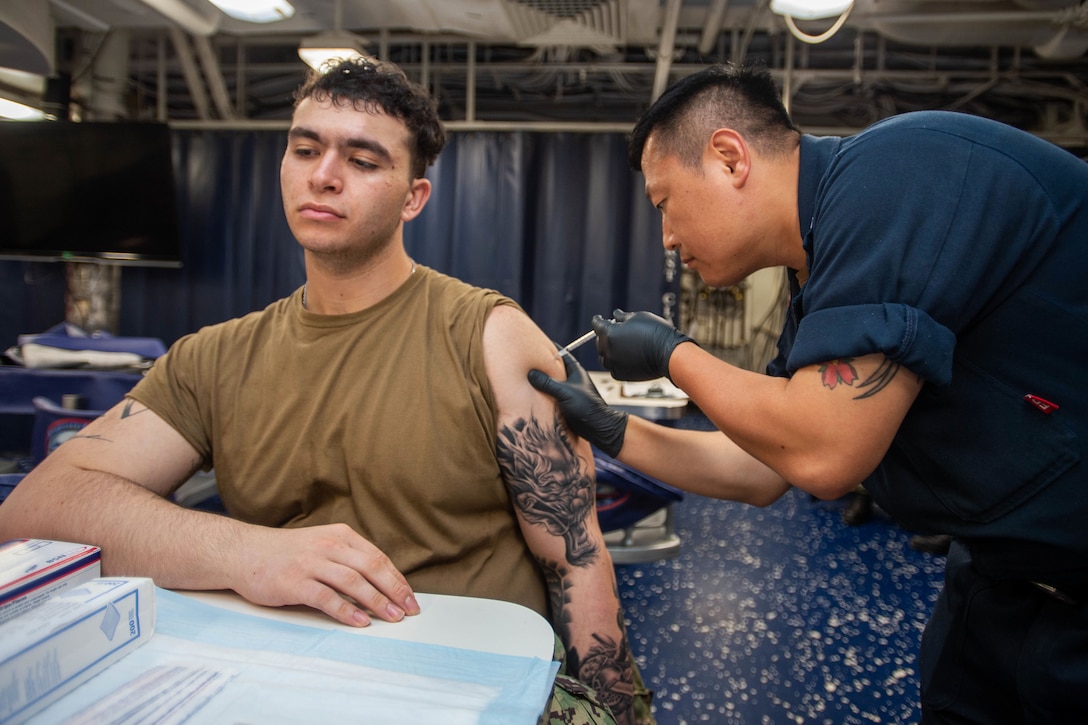 A service member wearing medical gloves bends down to administer an injection to a service member.