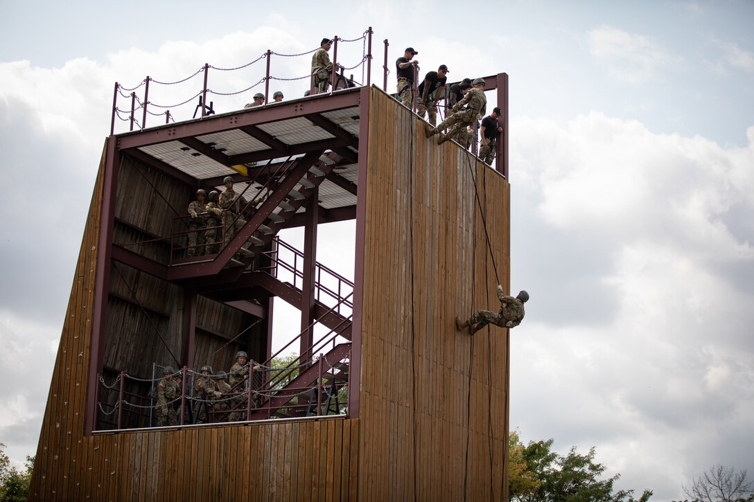 Soldiers and airmen line up to rappel down a wooden structure.