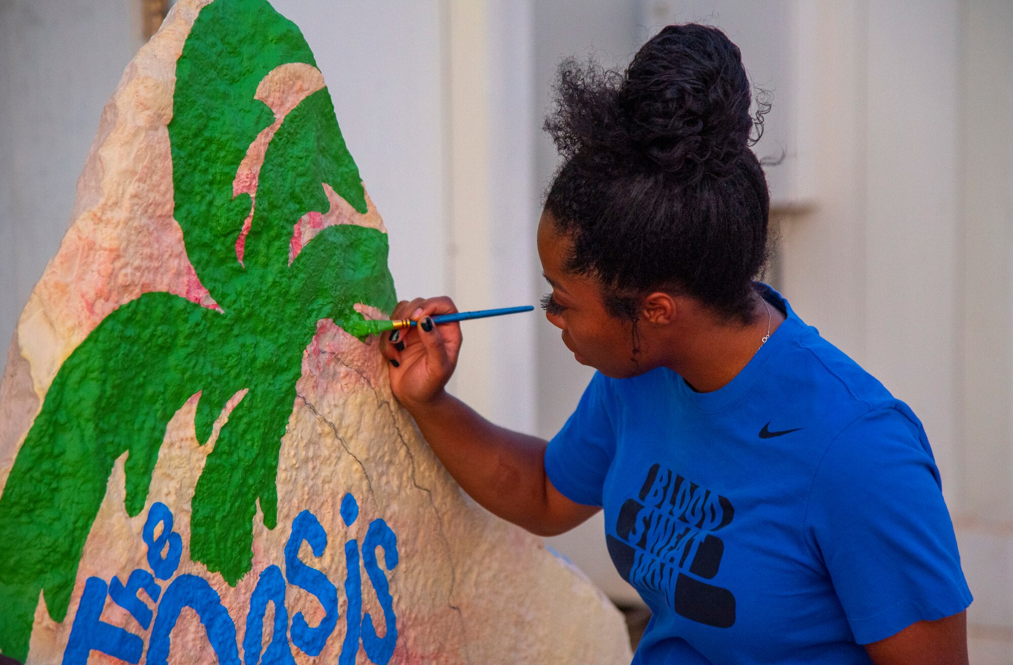 Staff Sgt. Jasmin Walker, 332d Wing Special Agencies, repaints a decorative rock mural in front of the Oasis at an undisclosed location in Southwest Asia, Sept. 4, 2022. The Oasis is a volunteer-run quiet area where Airmen can relax with snacks and other amenities. (U.S. Air Force photo by: Tech. Sgt. Jim Bentley)