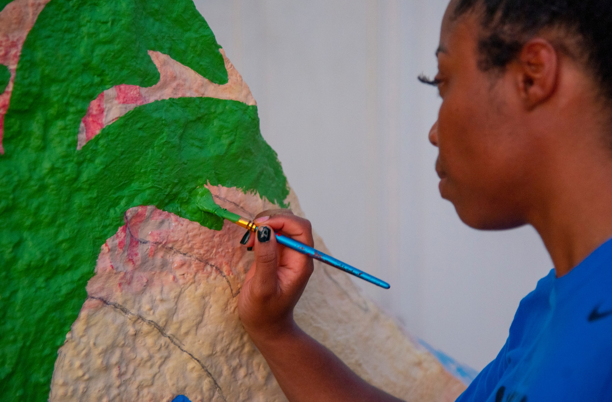 Staff Sgt. Jasmin Walker, 332d Wing Special Agencies, repaints a decorative rock mural in front of the Oasis at an undisclosed location in Southwest Asia, Sept. 4, 2022. The Oasis is a volunteer-run quiet area where Airmen can relax with snacks and other amenities. (U.S. Air Force photo by: Tech. Sgt. Jim Bentley)