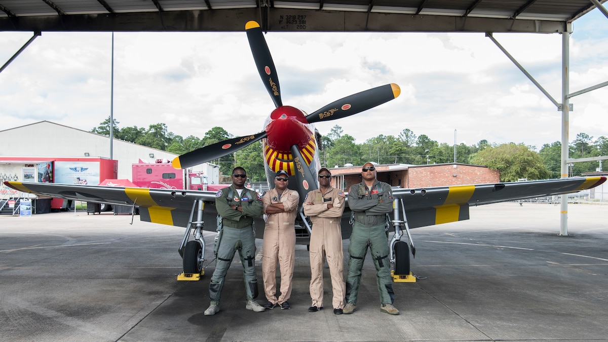 Maj. Paul "Loco" Lopez, U.S. Air Force F-22 Raptor Demonstration Team commander and pilot, Keith Charlot, an aviation photographer, Bradford Lang, the son of a Tuskegee Airman and pilot with the Commemorative Air Force, and Maj. Rich "Sheriff" Peace, an F-16 Fighting Falcon instructor pilot with the 100th Fighter Squadron, pose in front of a P-51 Mustang
