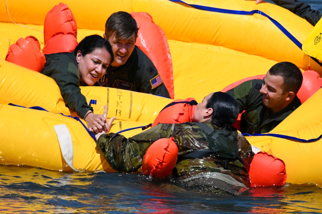 Three airmen sitting in an inflatable raft pull a fellow airman out of a body of water during training.