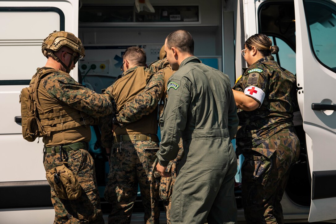 A U.S. Marine and a U.S. Navy Hospital Corpsman with 4th Air Naval Gunfire Liaison Company, Marine Forces Reserve, in support of Special Purpose Marine Air-Ground Task Force UNITAS LXIII, and Brazilian Air Force medical staff assist a marine into a hospital van during a simulated casualty evacuation during exercise UNITAS LXIII, Santa Cruz Air Force Base, Rio de Janeiro,  Sept. 7, 2022. 4th ANGLICO and the Brazilian Marine Corps tested the capability of transporting wounded marines by Brazilian military medical units. UNITAS trains forces to conduct joint maritime operations through the execution of anti-surface, anti-submarine, anti-air, amphibious and electronic warfare operations that enhance warfighting proficiency and increase interoperability among participating naval and marine forces. (U.S. Marine Corps photo by Cpl. Colton K. Garrett)