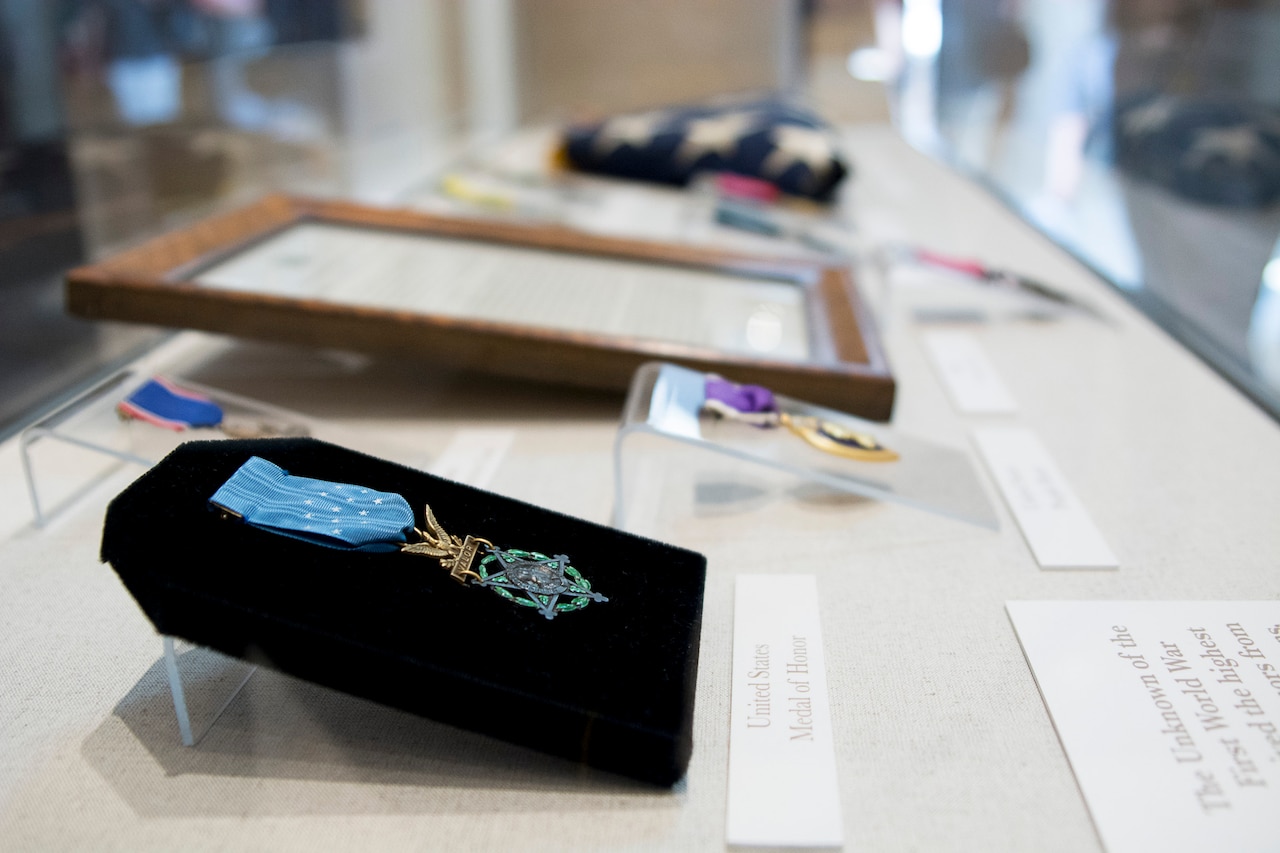 A medal is displayed on a stand in a case with other similar items.