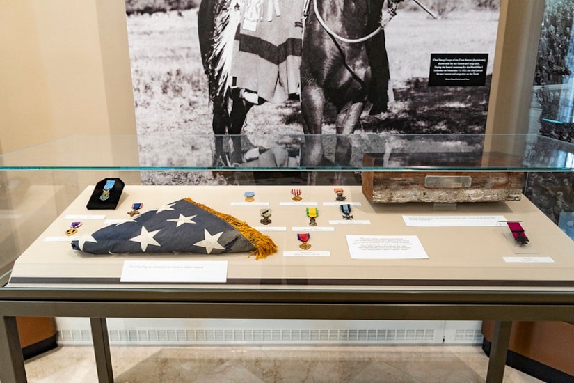 A folded U.S. flag and several medals are displayed inside a display case.