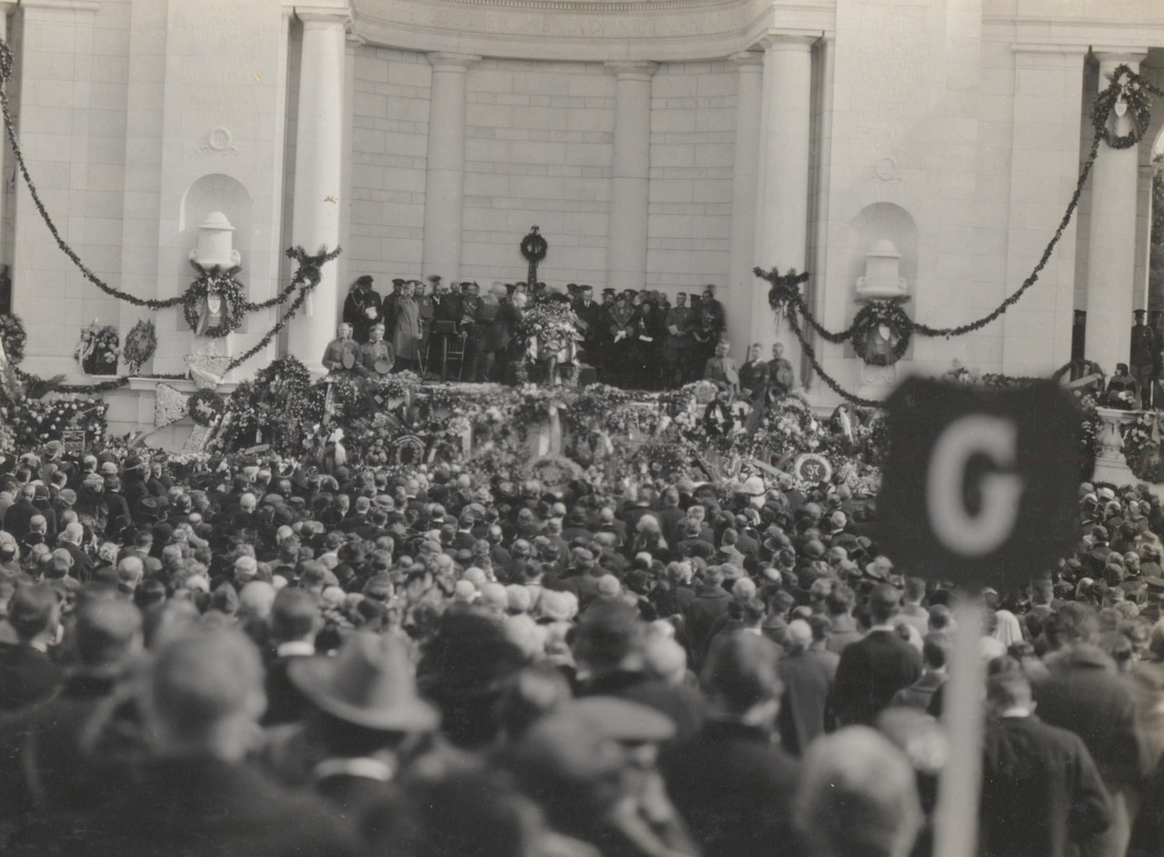 A massive crowd of people looks toward a podium, where a casket lies.