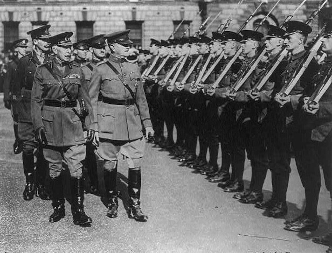 Several men look at a row of soldiers with rifles slung over their shoulders.