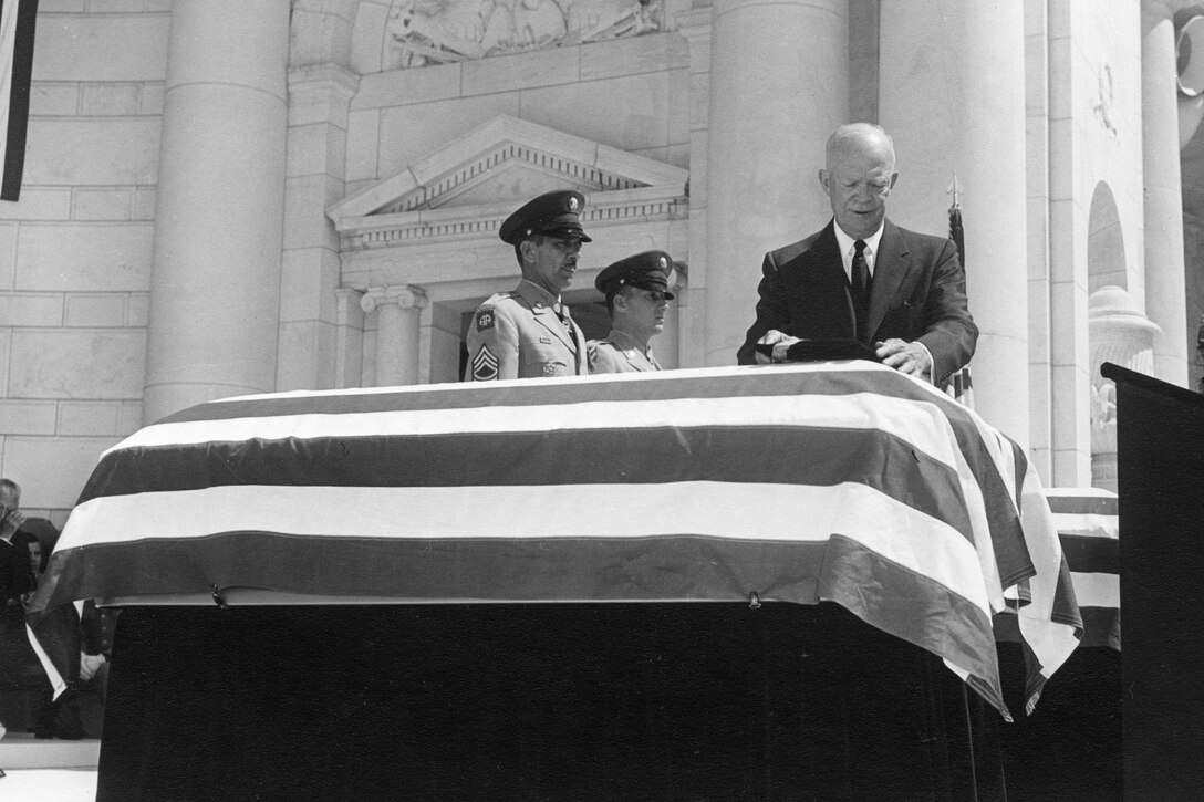 A man places an object on a flag-draped casket.