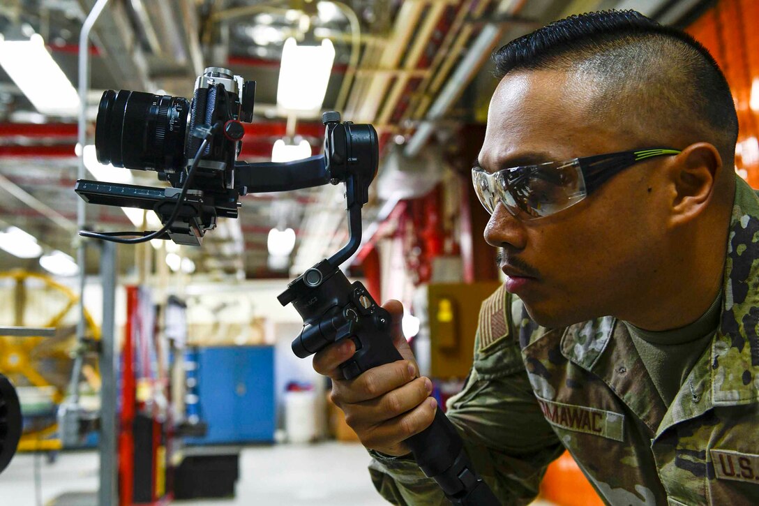 An airman looks into the viewfinder of a camera.