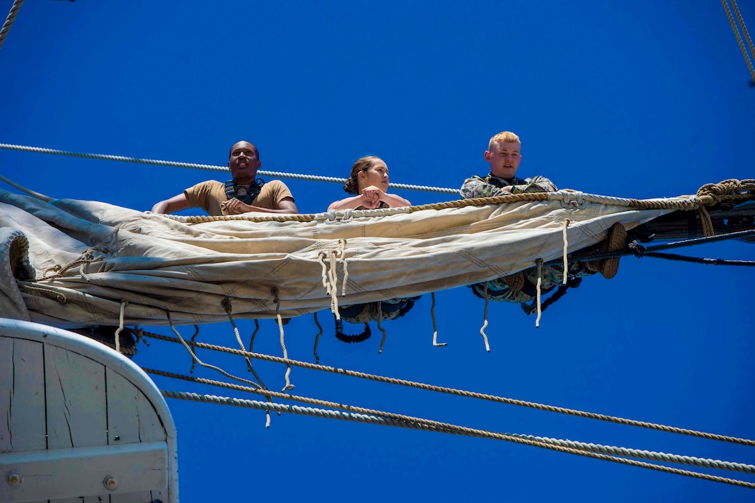 Three sailors work on the sails of a ship.