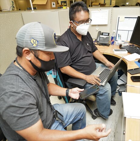 Daniel Bumanglag, right, an information technology specialist with Pearl Harbor Naval Shipyard and Intermediate Maintenance Facility (PHNSY & IMF) Cellular Device Team, uses a newly acquired laptop to update a customer’s government mobile phone. Currently, PHNSY & IMF has received more than 3,800 new and faster desktops and laptops since February 2021 and is scheduled to refresh the remaining 1,200 computers by the end of 2022. (Official U.S. Navy photo by Marc Ayalin)