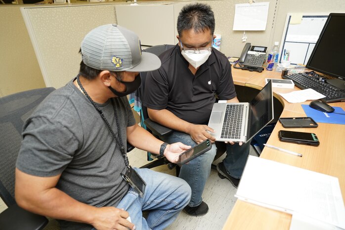 Daniel Bumanglag, right, an information technology specialist with Pearl Harbor Naval Shipyard and Intermediate Maintenance Facility (PHNSY & IMF) Cellular Device Team, uses a newly acquired laptop to update a customer’s government mobile phone. Currently, PHNSY & IMF has received more than 3,800 new and faster desktops and laptops since February 2021 and is scheduled to refresh the remaining 1,200 computers by the end of 2022. (Official U.S. Navy photo by Marc Ayalin)