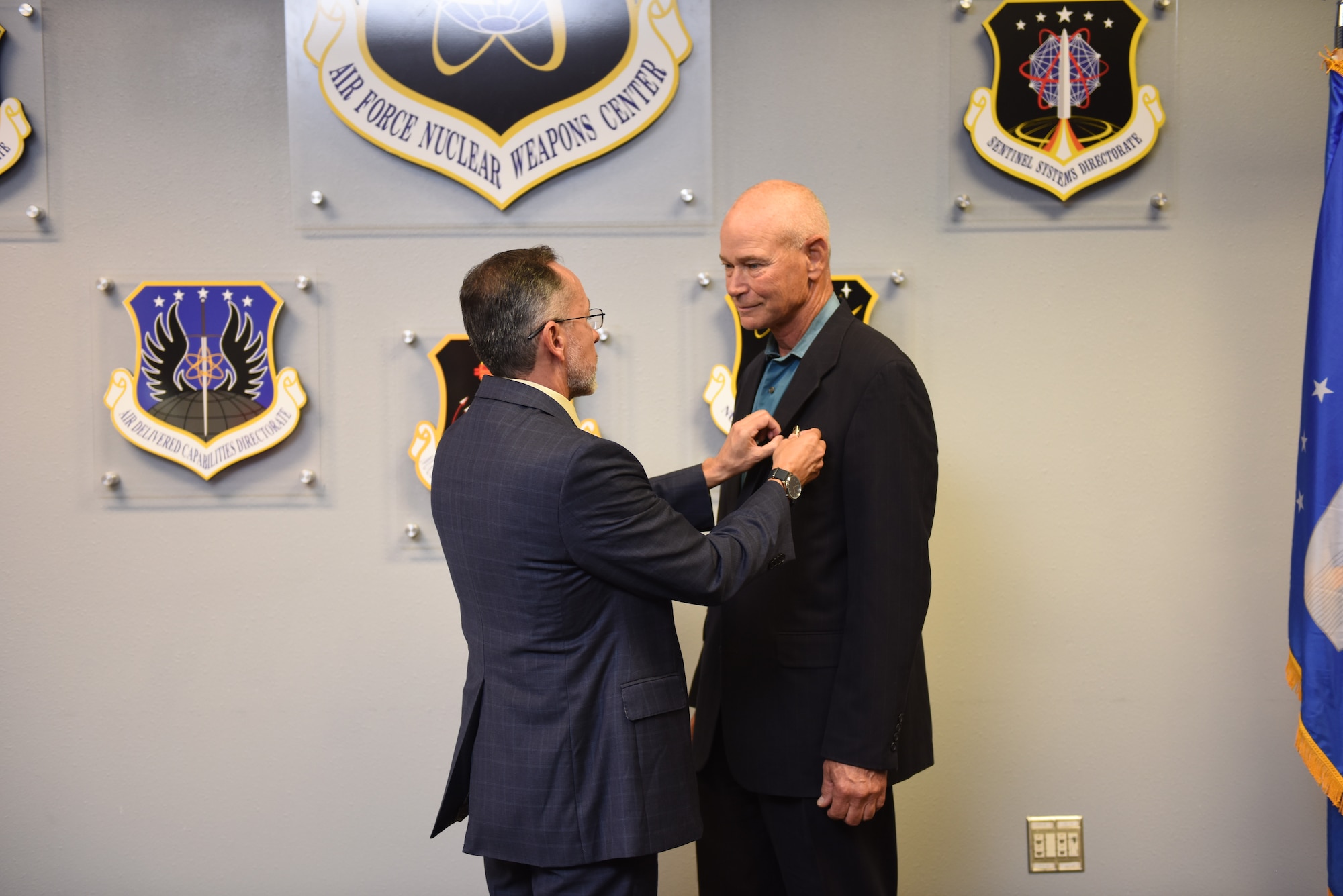 One man pins something on the lapel of another man's suit