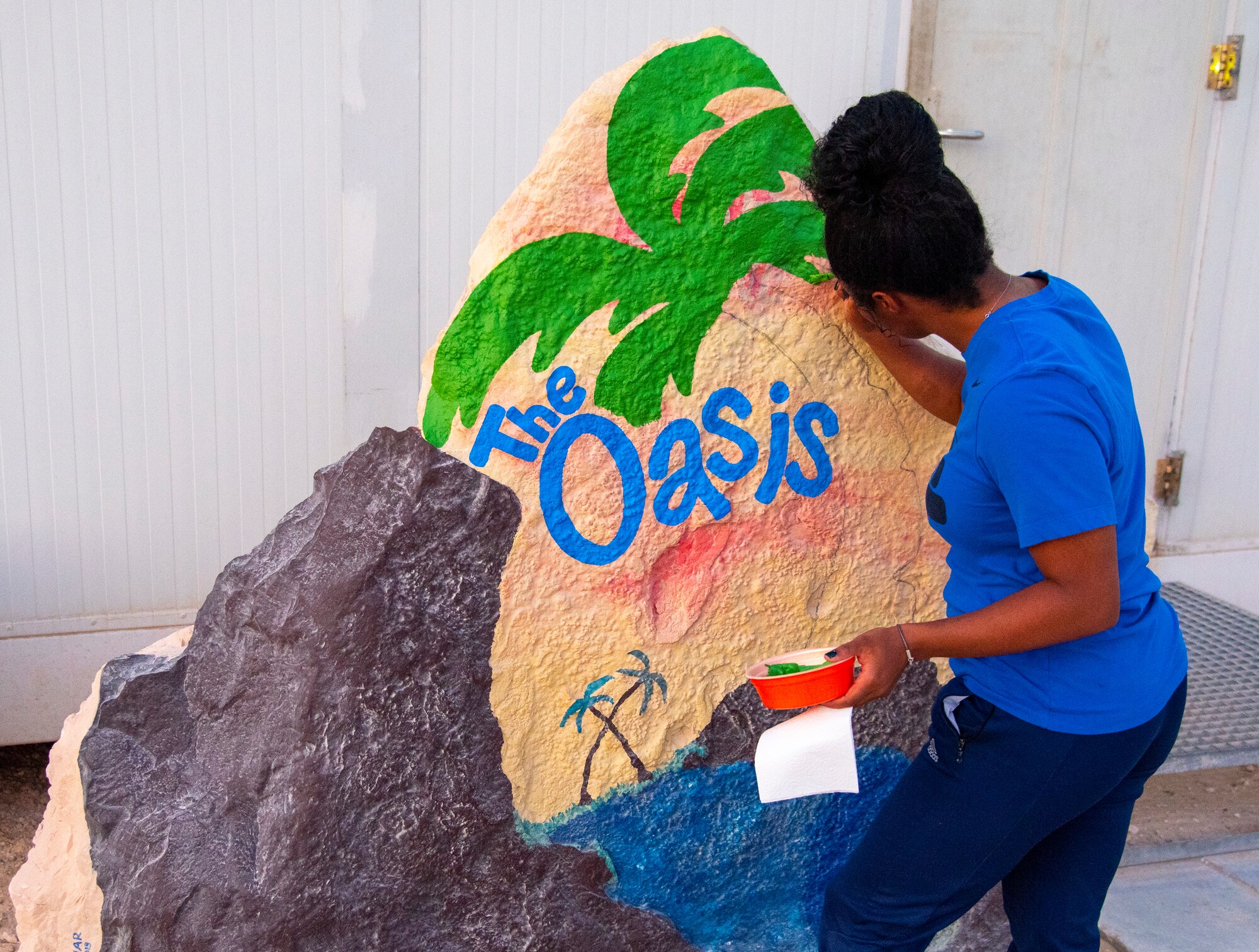 Staff Sgt. Jasmin Walker, 332d Wing Special Agencies, repaints a decorative rock mural in front of the Oasis at an undisclosed location in Southwest Asia, Sept. 4, 2022. The Oasis is a volunteer-run quiet area where Airmen can relax with snacks and other amenities. (U.S. Air Force photo by: Tech. Sgt. Jim Bentley)