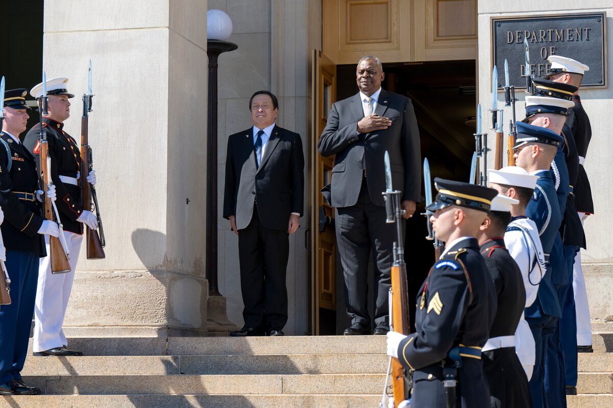 Two men gather on the steps on the Pentagon as service member carrying rifles stand in parallel lines.