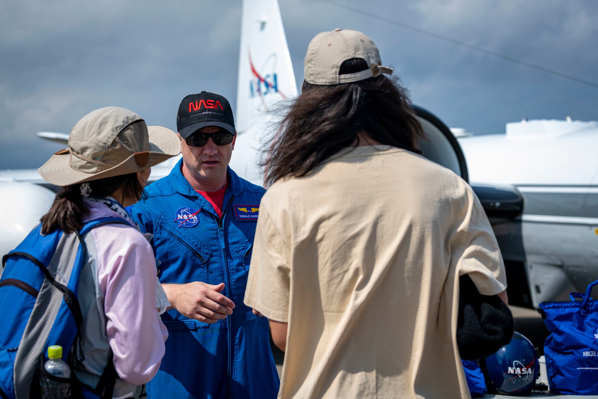 Attendees talk and ask questions with NASA member in flight suit in front of an aircraft.
