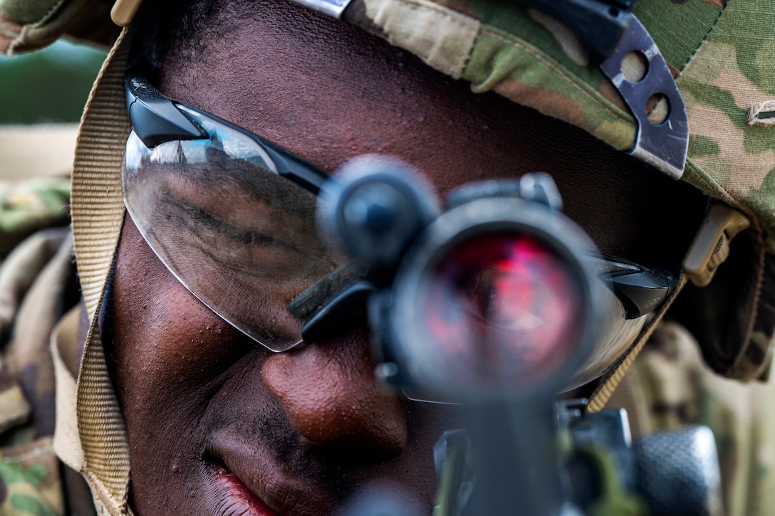 A uniformed service member looks through the sight of a weapon.