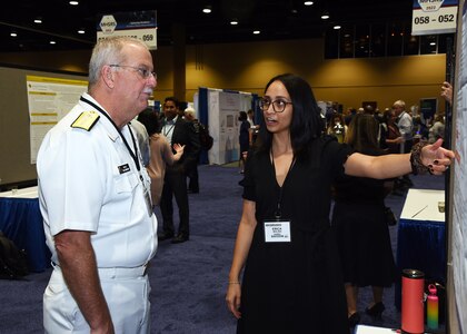 KISSIMMEE, Fla. – (Sept. 13, 2022) – Dr. Erica Molina, of San Antonio, a research scientist assigned to Naval Medical Research Unit (NAMRU) San Antonio, briefs the Surgeon General of the Navy, Rear. Adm. Bruce L. Gillingham during a poster session held on day two of the 2022 Military Health System Research Symposium (MHSRS) held at the Gaylord Palms Resort and Convention Center. The 2022 MHSRS brings together military, government, academia, and industry experts for four days of critical conversations and intensive idea sharing. Presenters will share their latest research findings and challenges on topics including combat casualty care, military operational medicine, clinical and rehabilitative medicine, medical simulation and information sciences, military infectious diseases, and the radiation health effects. NAMRU San Antonio is one of the leading research and development laboratories for the U.S. Navy under the Department of Defense and is one of eight subordinate research commands in the global network of laboratories operating under the Naval Medical Research Center in Silver Spring, Md.  Its mission is to conduct gap driven combat casualty care, craniofacial, and directed energy research to improve survival, operational readiness, and safety of DOD personnel engaged in routine and expeditionary operations. (U.S. Navy photo by Burrell Parmer, NAMRU San Antonio Public Affairs/Released)