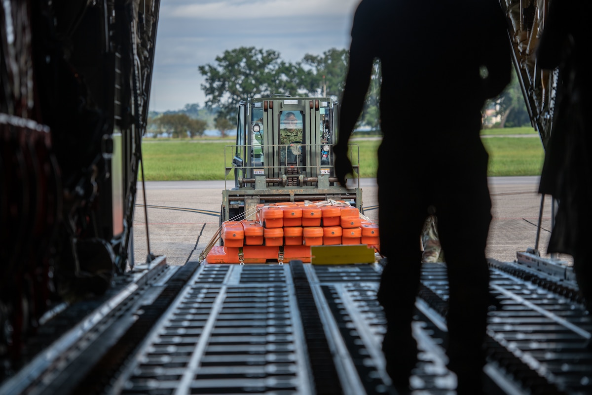A forklift carrying cargo waits behind a C-130J aircraft