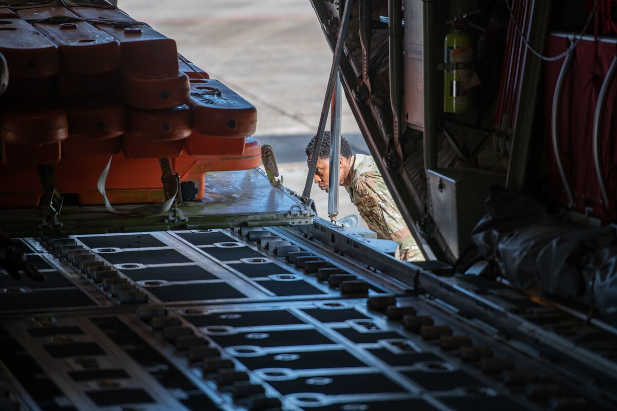 An airmen gets eye level with a pallet being loaded onto the ramp of a C-130J