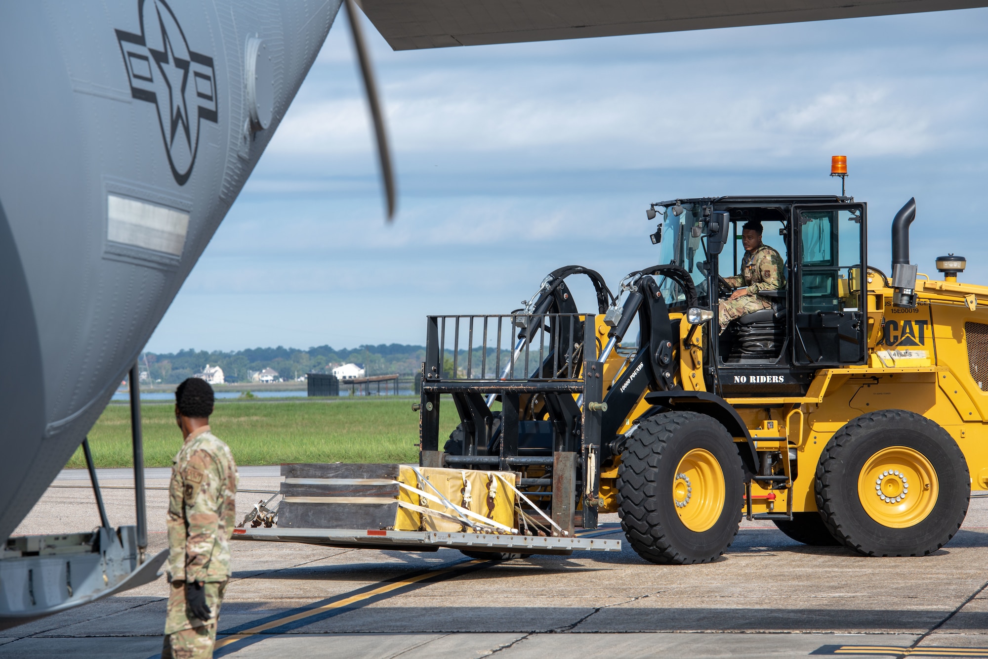 An Airman steers a forklift carrying cargo toward a C-130J aircraft