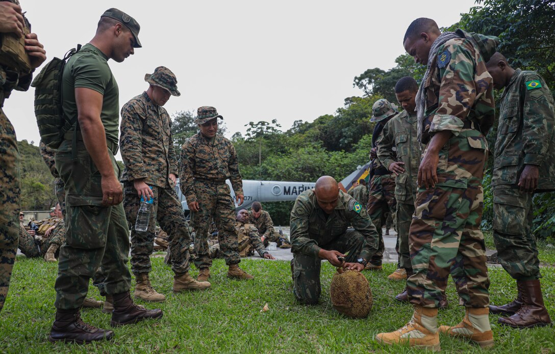 A Brazilian marine cuts open fruit while marines from the Dominican Republic and the United States of America watch during exercise UNITAS LXIII in Ilha do Governador, Rio de Janeiro, Sept. 5, 2022. UNITAS is the world’s longest-running annual multinational maritime exercise that focuses on enhancing interoperability among multiple nations and joint forces during littoral and amphibious operations in order to build on existing regional partnerships and create new enduring relationships that promote peace, stability and prosperity in the U.S. Southern Command’s area of responsibility. (U.S. Marine Corps photo by Lance Cpl. Trystan Taft)