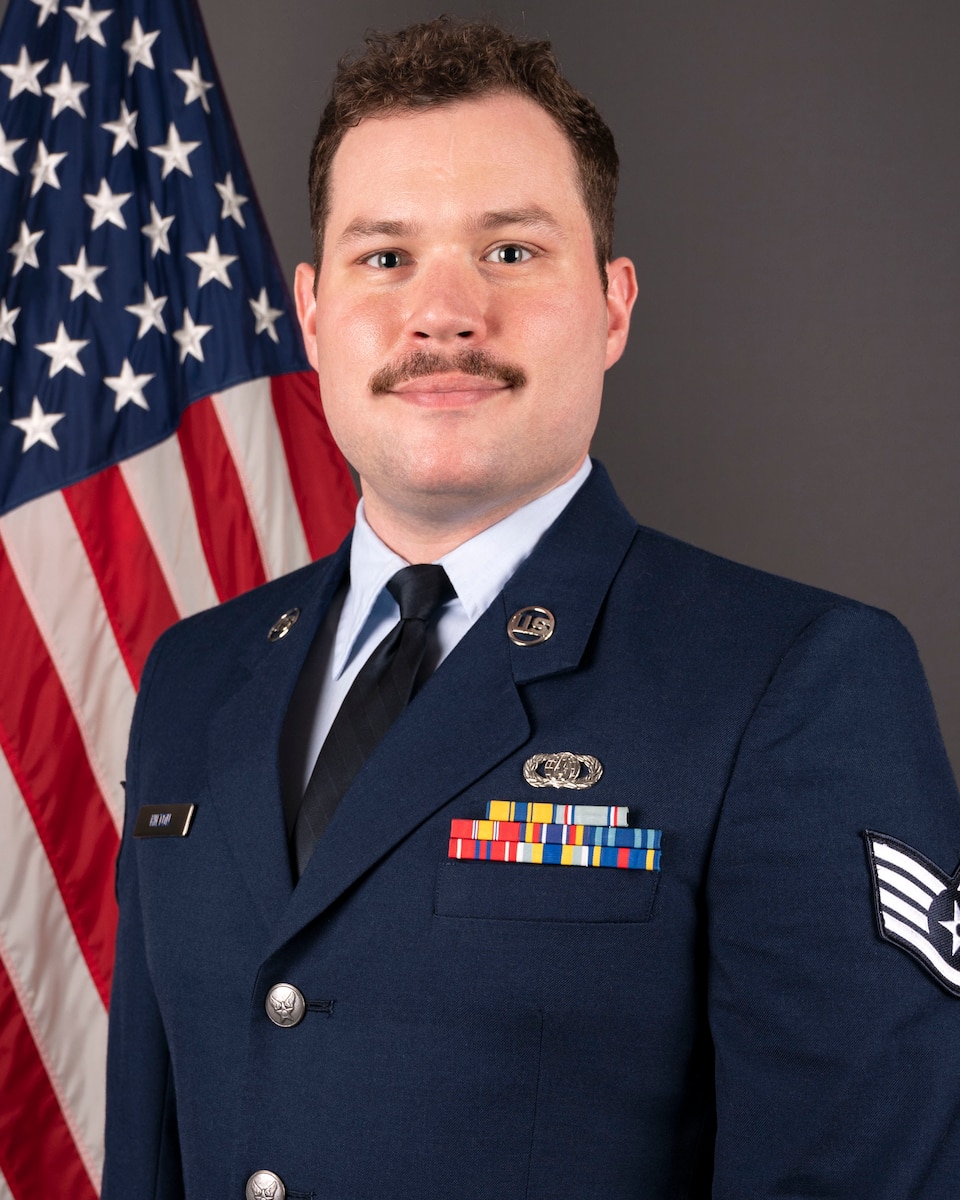 An official headshot photo of SSgt Jacob Hilton in front of the American flag. He is wearing the blue service dress uniform.