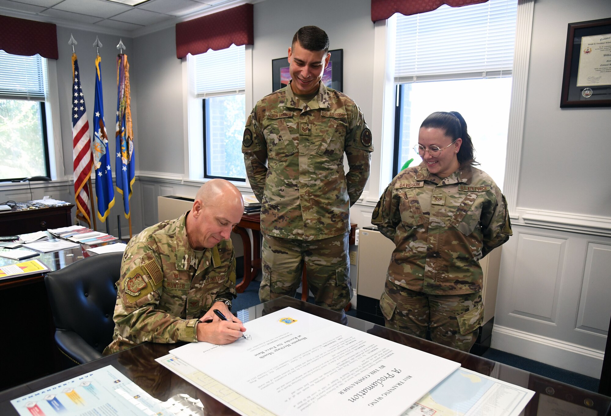 U.S. Air Force Col. William Hunter, 81st Training Wing commander, signs the Hispanic Heritage Month proclamation as Tech. Sgt. Hernan Negron Santiago and Staff Sgt. Danielle Davidson, 334th Training Squadron instructors, stand by inside the 81st TRW headquarters building at Keesler Air Force Base, Mississippi, Sept. 14, 2022. Hispanic Heritage Month is celebrated September 15 through October 15. (U.S. Air Force photo by Kemberly Groue)