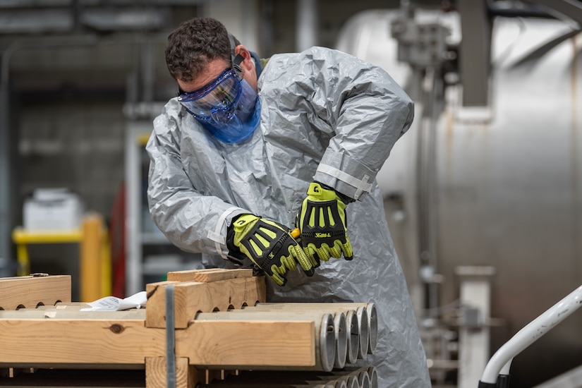 A man in personally protective equipment pries wood off a rack of rockets.