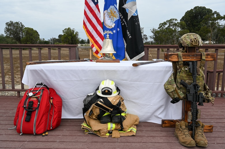 First responders and military gear ceremoniously displayed in front of table and flags
