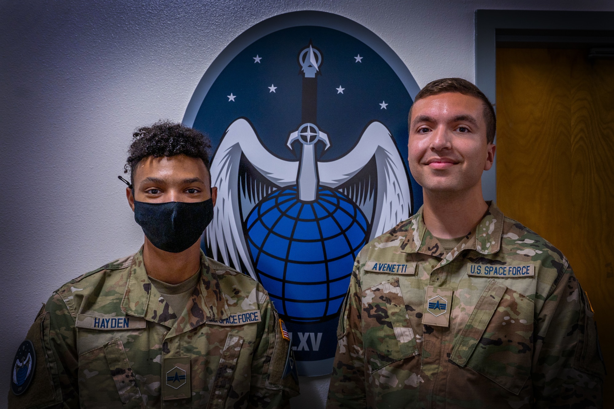 Spec. 3 Jesse Hayden, left, and Spec. 4 Derek Avenetti, both 65th Cyberspace Squadron cyber operators, stand in front of their unit’s emblem at Vandenberg Space Force Base, Calif., Sept. 9, 2022. Hayden and Avenetti performed life-saving treatment to a military member Aug. 16, 2022, during a physical training test. (U.S. Space Force photo by Tech. Sgt. Luke Kitterman)