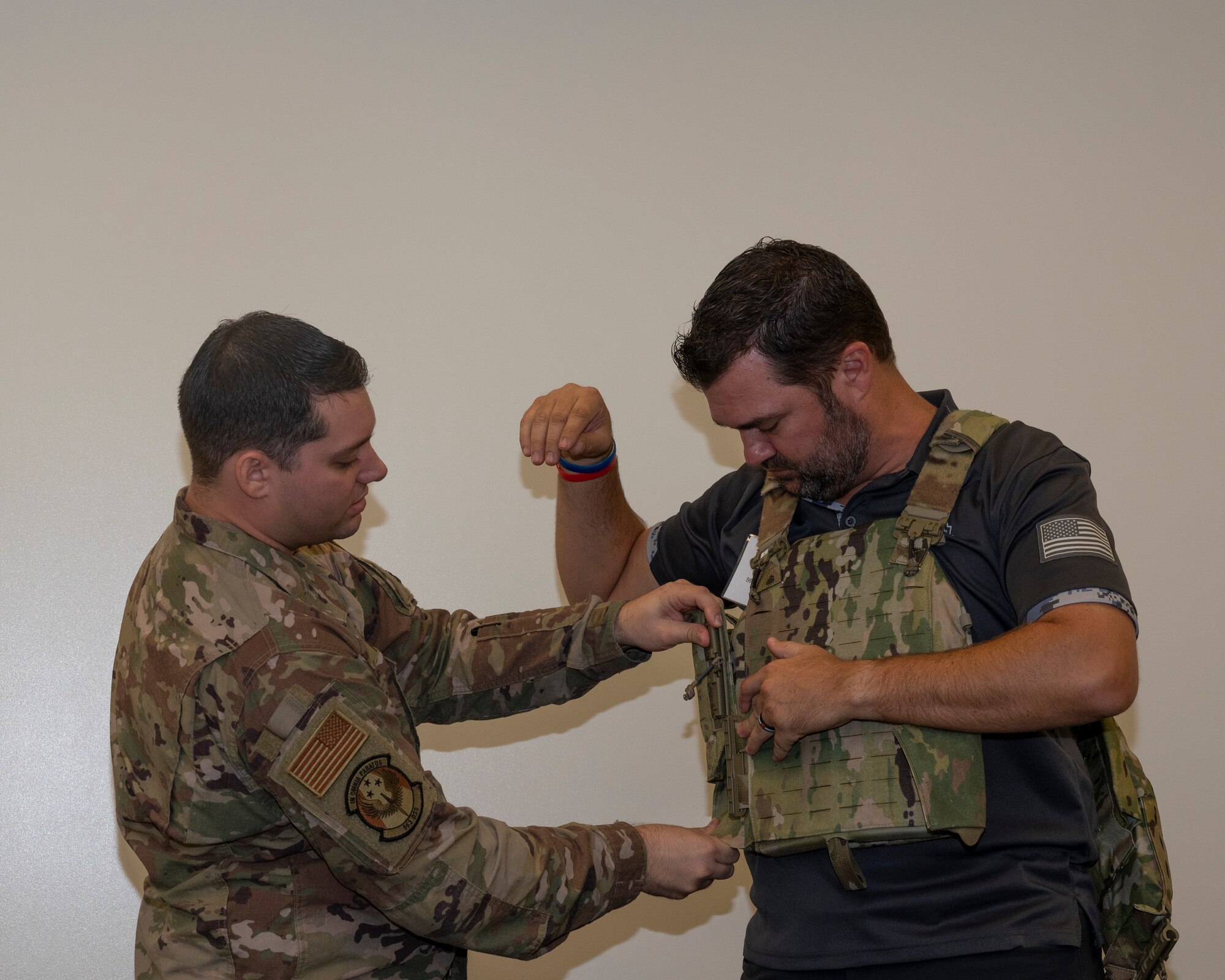 A picture of a man helping another put on a vest