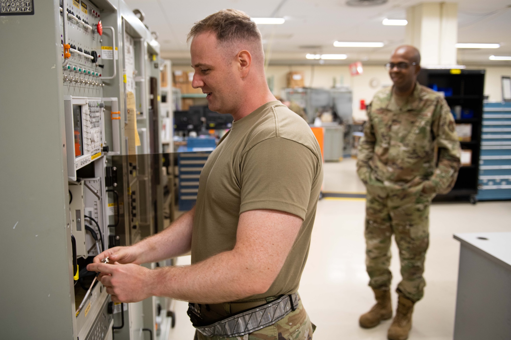 A supervisor watches as an Airman runs through the wires on an electronic unit