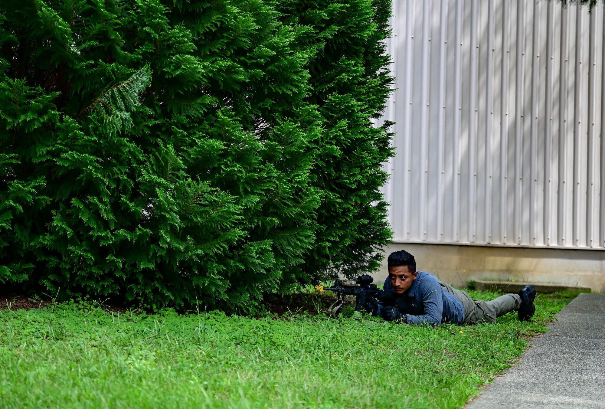 Man lying in grass with weapon.