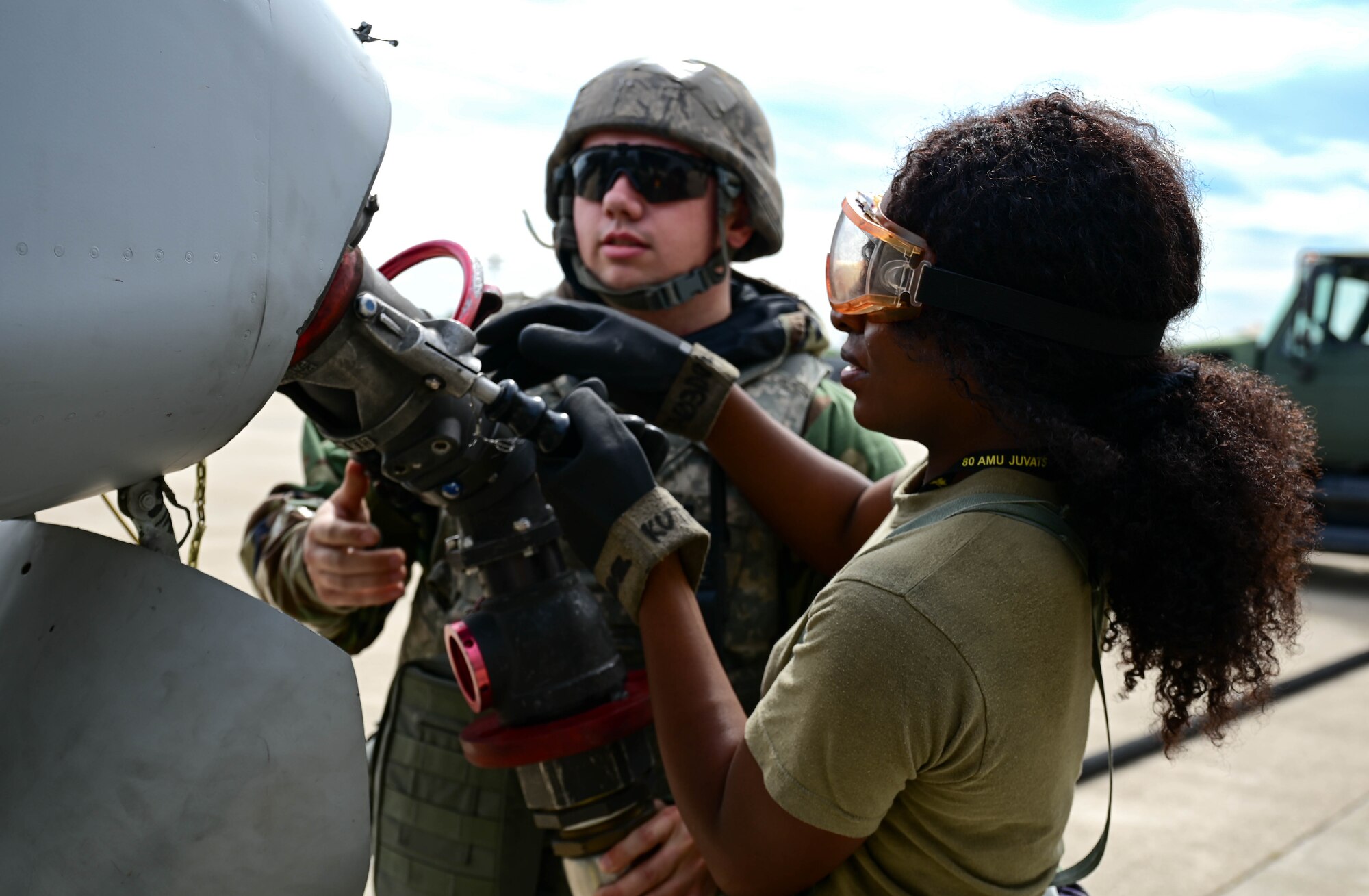 Two people attaching fuel hose to aircraft.