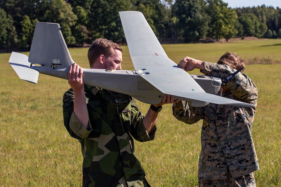 Two uniformed service members hold and examine a drone while standing in a field.