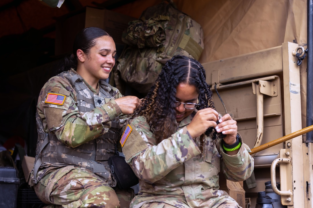 One female soldier helps style the hair of another female soldier.