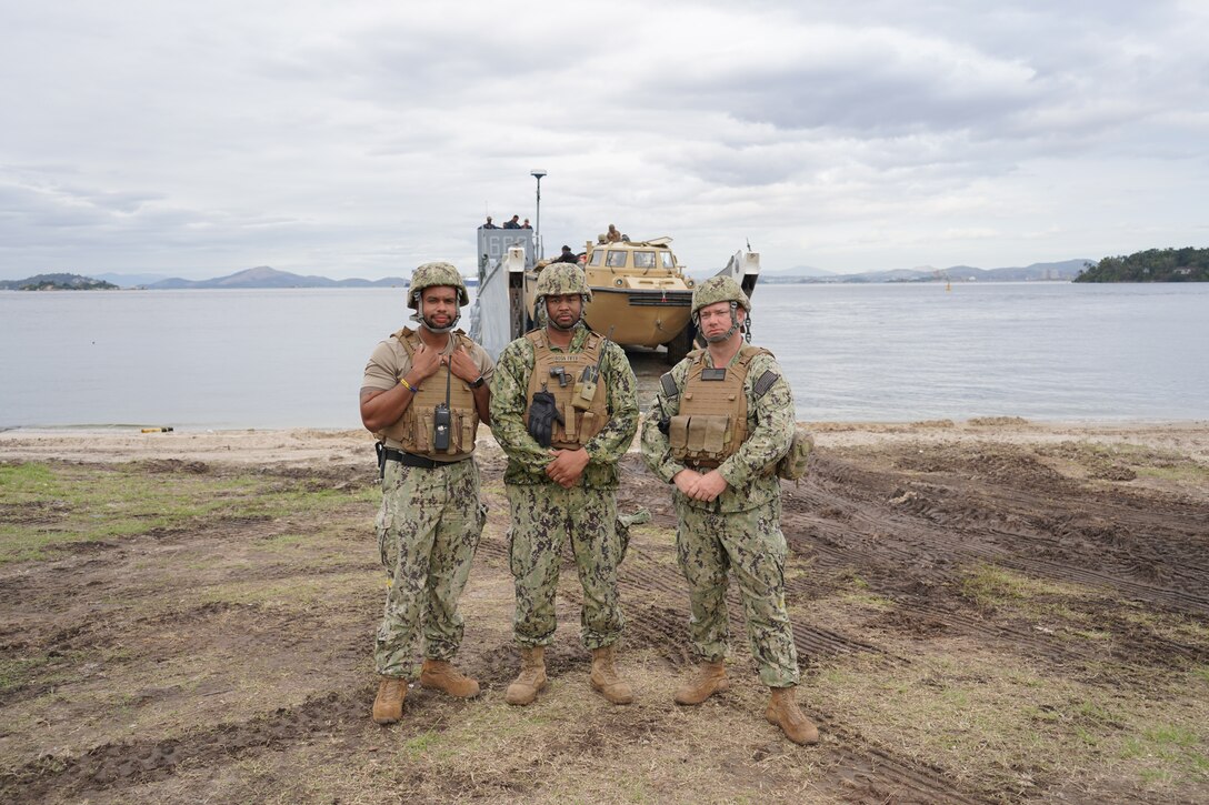 From left, Boatswain’s Mate 3rd Class Ali Fayyad, Chief Warrant Officer Michael Fifer, and Engineman 1st Class Jason Hook from Command Beachmaster Unit (BMU) 2, Expeditionary Strike Group (ESG) 2, United States Navy, pose for a photograph after loading their vehicles and equipment aboard Landing Craft, Utility 1663 at Ilha do Governador, Rio de Janeiro, Sept. 6, 2022.  BMU-2 functions as the beach traffic controller and provides craft landing zone beach party teams in support of ship-to-shore movement to facilitate landing of personnel and equipment. They also provide a salvage capability with Light Amphibious Recovery Craft (LARC) which is essential to the safety and success of the various amphibious operations throughout Brazil. UNITAS, which is Latin for ‘unity,’ trains forces from across the globe in South America to conduct joint maritime operations through the execution of anti-surface, anti-submarine, anti-air, amphibious, and electronic warfare operations that enhance warfighting proficiency and increase interoperability among participating navy and marine forces. (U.S. Marine Corps photo by Maj. Jeremy Wheeler)